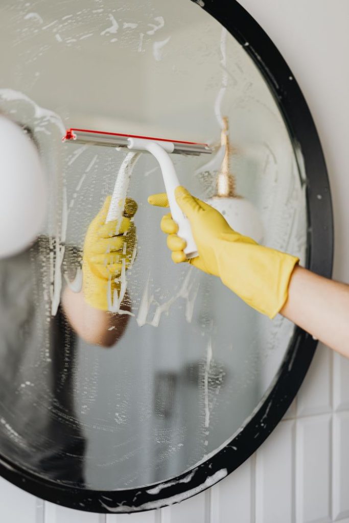 anonymous-man-cleaning-mirror-in-bathroom-4239139 Faceless housekeeper in yellow rubber gloves cleaning round mirror from foam by squeegee in bathroom